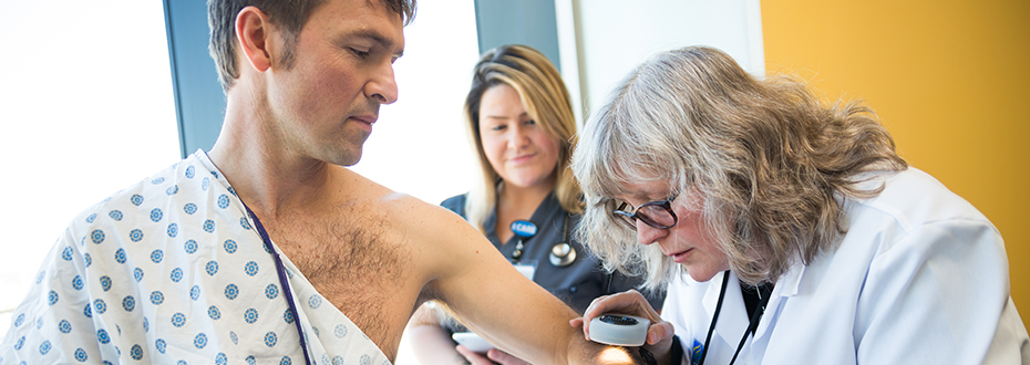 Dr. Sancy Leachman (right) uses a magnifying device to examine a patient's skin.