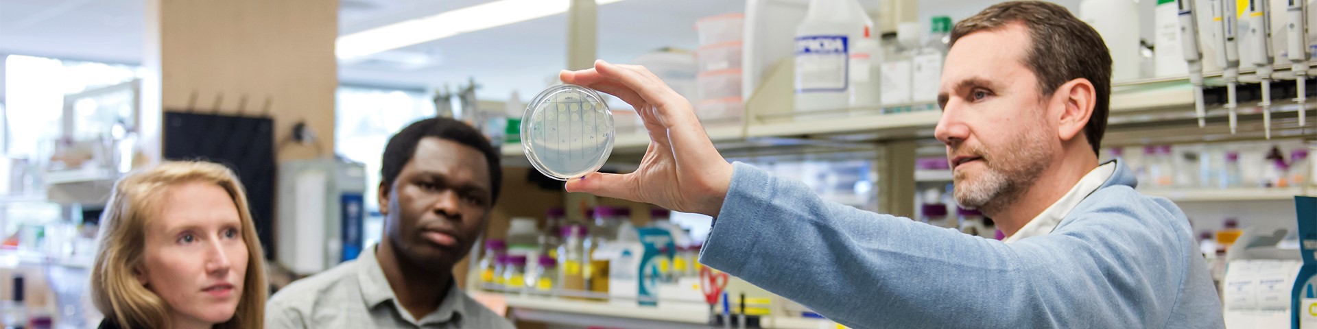 Photo of a scientist showing students a petri dish