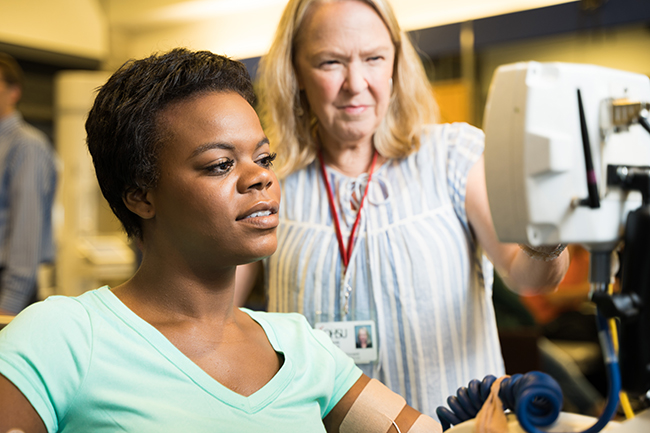 A woman working with a computer as part of her neurologic rehabilitation, with her provider standing over her shoulder.
