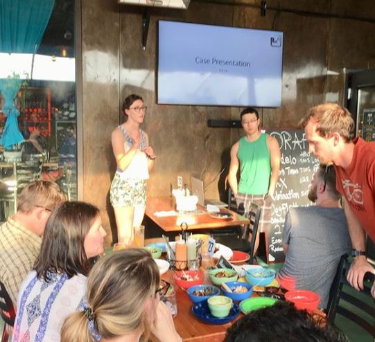 A resident and Faculty member speaking in front of an audience in a casual restaurant setting.