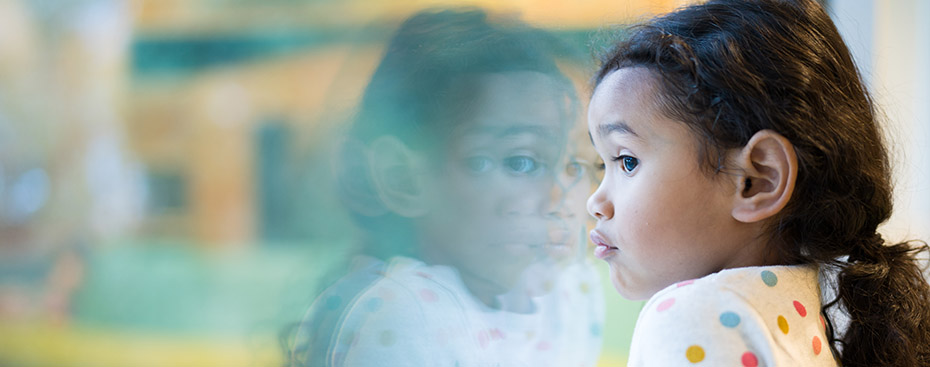 Photo of a girl looking through a window, we see her face and her reflection