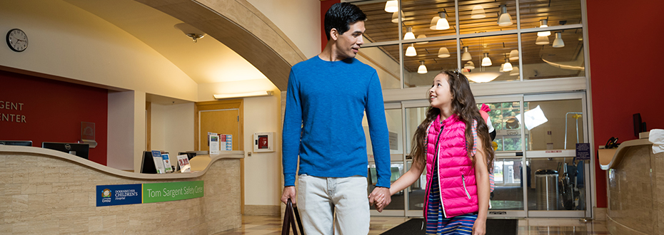 A father holding his daughter's hand while they walk through the Doernbecher Children's Hospital lobby.