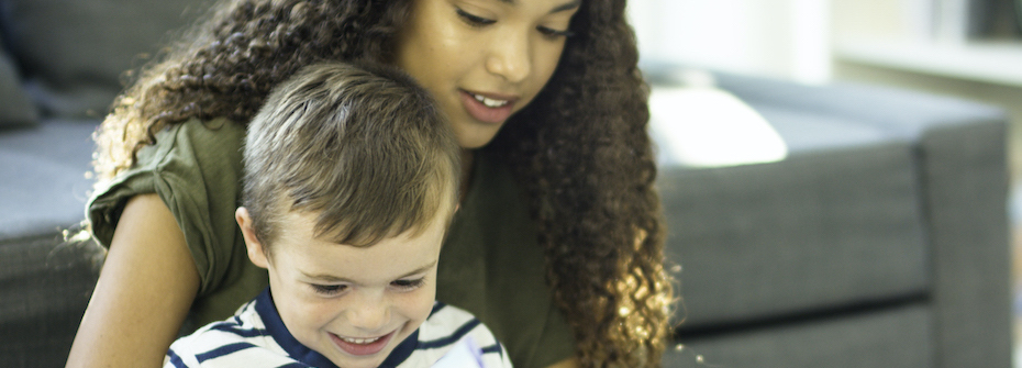 Photo of a smiling child sitting with a teenage babysitter