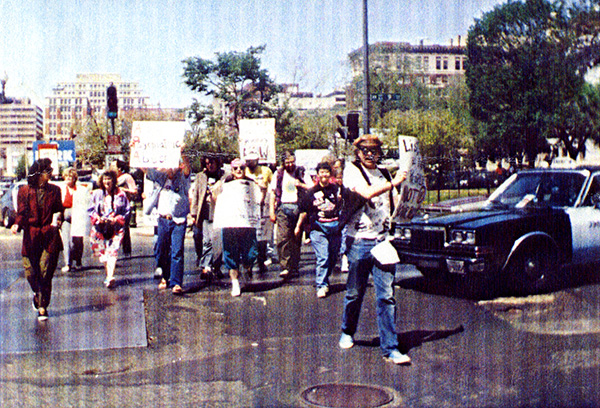 Color photoraph of people marching across a street with banners