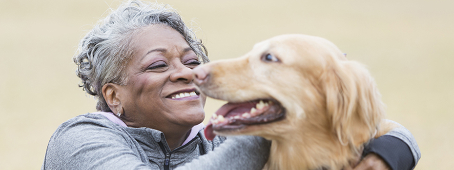 A woman smiling with her arm wrapped around a golden retriever dog.