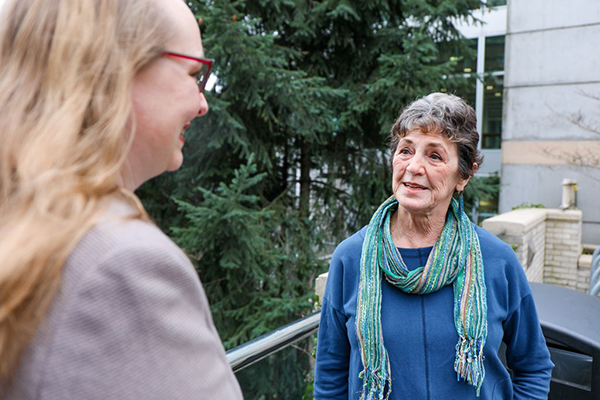 A woman speaking to another woman on a front porch.