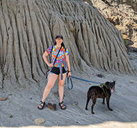 A woman smiling while hiking with her dog.