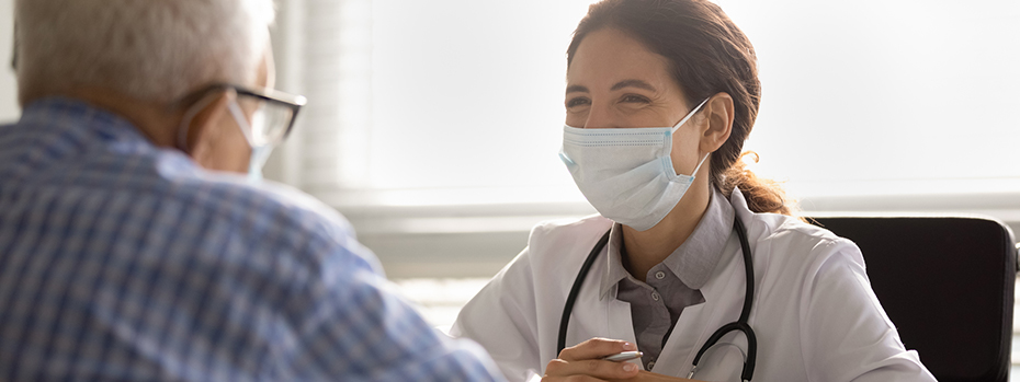 A woman doctor wearing a mask gives a warm facial expression to an older male patient in a clinic setting.
