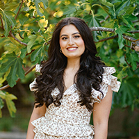 A woman smiling outside in front of lush foliage.