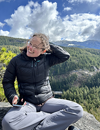 A woman smiling sitting atop a rock in the mountains.