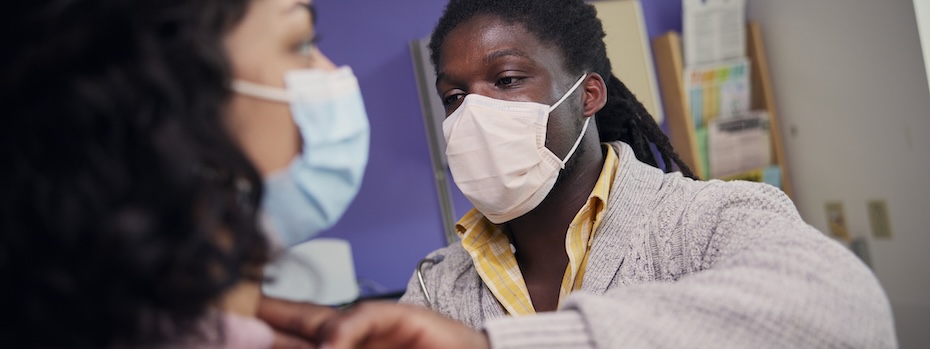 Mortuma Murry uses two fingers to check a young adult’s neck during a physical exam at OHSU.
