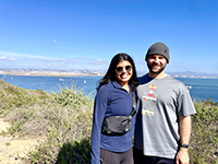 Two people smiling in the sun near water.