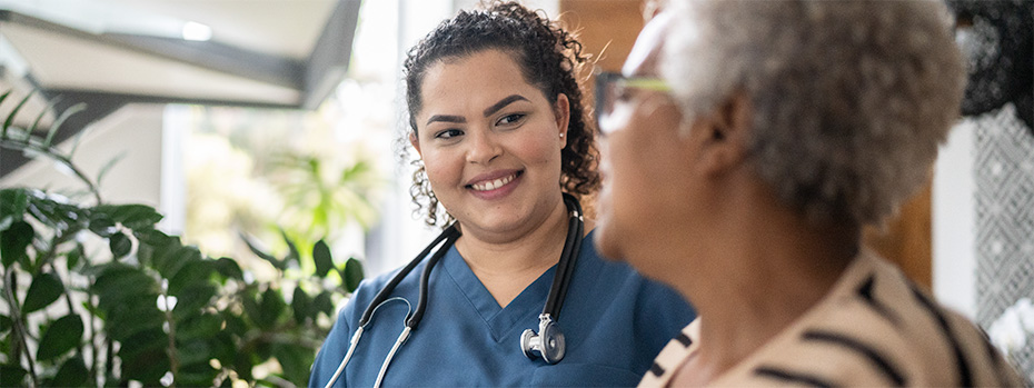 A student in blue scrubs wearing a stethoscope speaks with a patient.