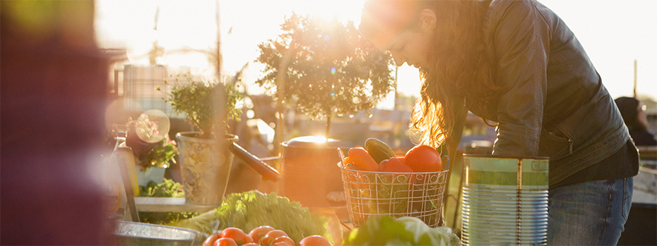 Person tending to an outdoor garden at sunset, with fresh vegetables and produce in baskets.