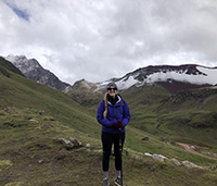 A woman standing on a hillside smiling on a cloudy day with mountains visible behind her.