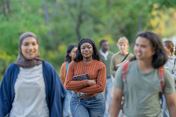 A student, holding a notebook, walks through a crowd.