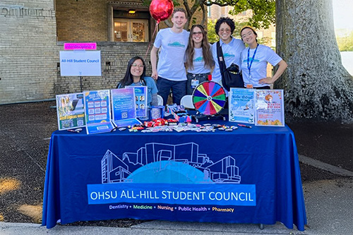 A group of members pose behind an All-Hill Student Council information table.