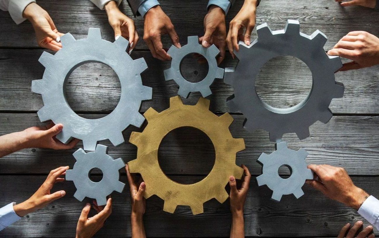 Interlocking gear shapes held by multiple hands, representing coordinated systems and collaboration