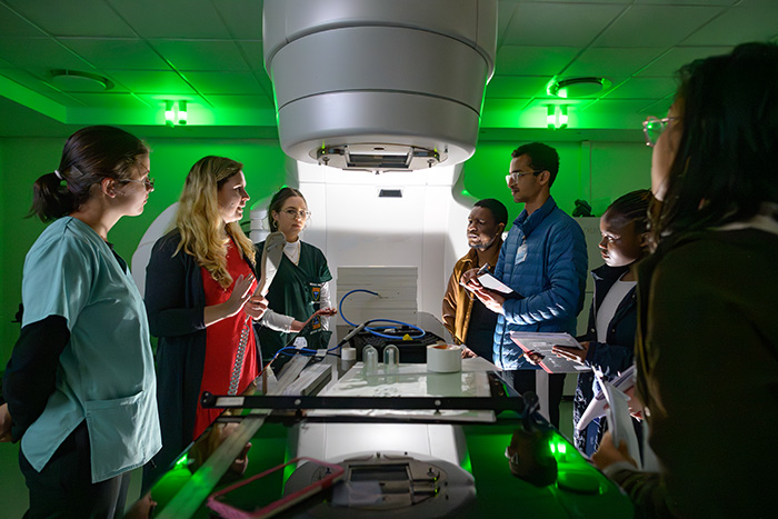 A group of medical physics students and professionals gathered around a linear accelerator during a training session.