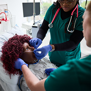 OHSU nursing students in scrubs perform a simulated airway procedure on a patient manikin in a clinical skills lab setting.
