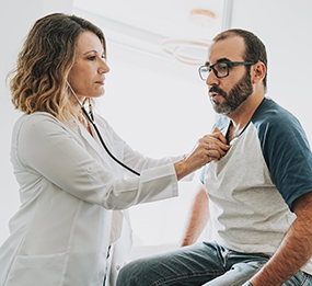 A female doctor uses a stethoscope to listen to a male patient’s heartbeat.