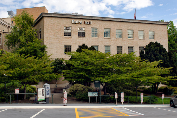 Brick building with windows and trees and a parking lot in front of it